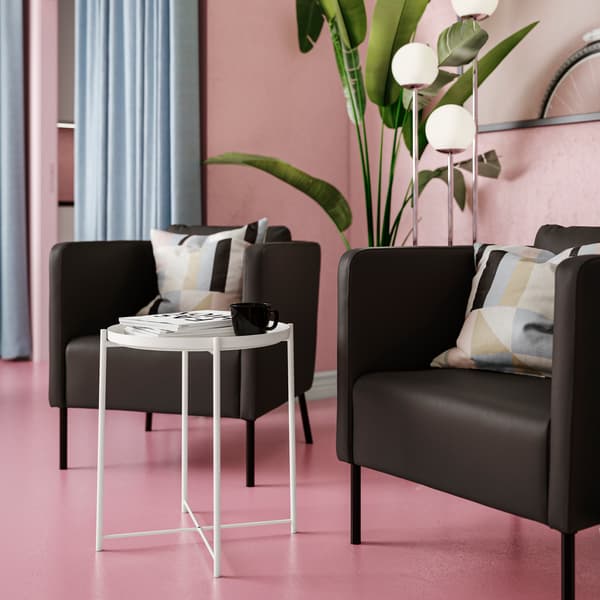 Dwa kubełkowe fotele EKERÖ w nowoczesnym stylu z pokryciem z tkaniny imitującej skórę ustawione w różowym pomieszczeniu przy okrągłym stoliku z tacą.