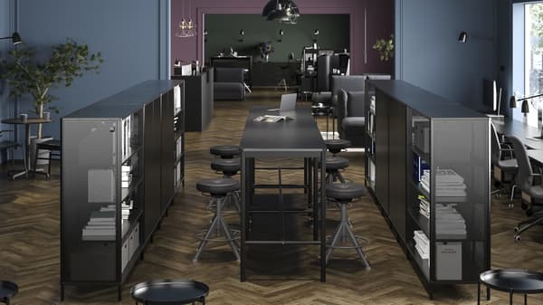 Dwa rzędy ustawionych na środku pomieszczenia czarnych regałów BEKANT z biurkami BEKANT i stołkami kreślarskimi TROLLBERGET pomiędzy nimi.