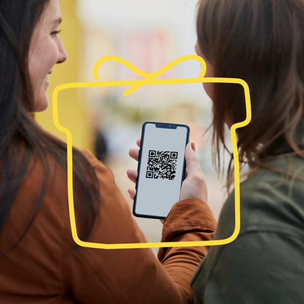 Dwie kobiety, jedna trzumająca telefon z wyświetlonym QR kodem.