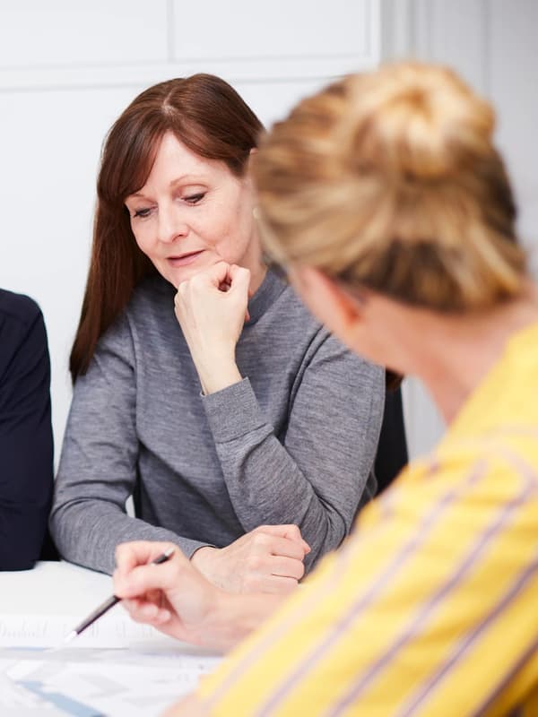 Dwie kobiety rozmawiają przy biurku nad dokumentami.
