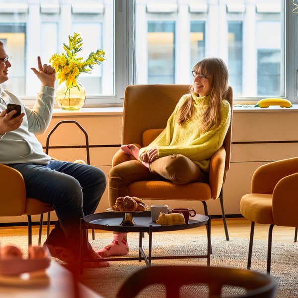 Dwie osoby rozmawiają w nowoczesnym biurze, siedząc na pomarańczowych fotelach przy stoliku.