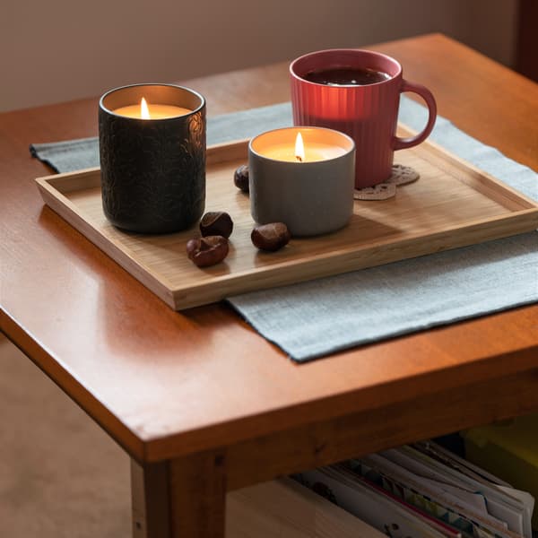 Dwie zapalone świece apachowe oraz kubek herbaty w ciemnoróżowym kubku, stojące na bambusowej tacy OSTBIT.