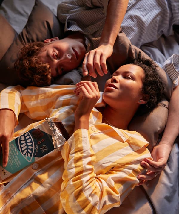 Dwoje studentów leży na łóżku i je tabliczkę czekolady.