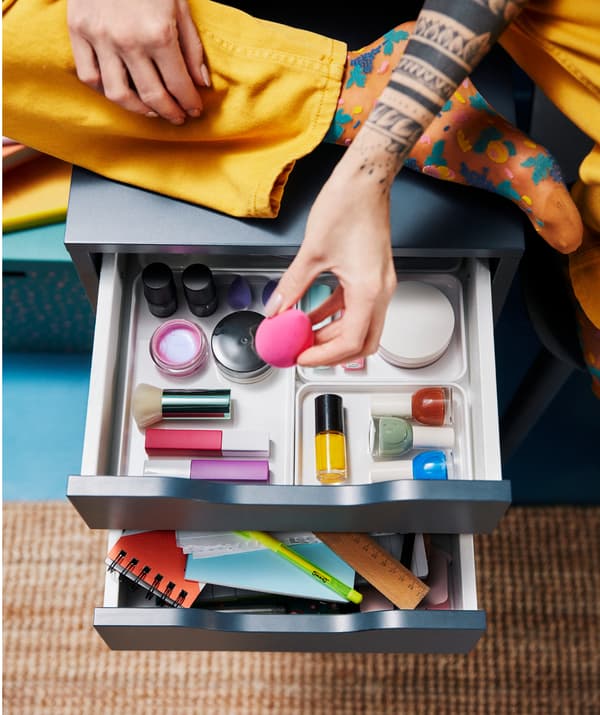 Dziewczyna z tatuażami siedzi na komodzie i bawi się kosmetykami do makijażu.