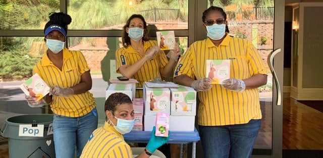 Four IKEA co-workers in uniform wearing face masks and holding IKEA products in front of glass windows.
