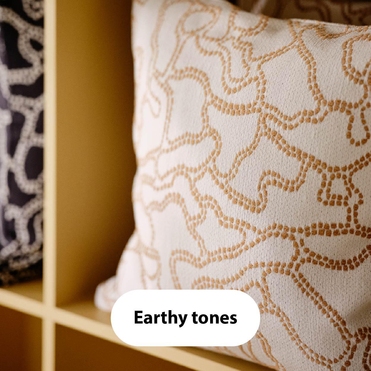 Earthy tones – Close-up of decorative pillows in beige and white with organic line patterns, placed in a golden-toned cubby shelf.