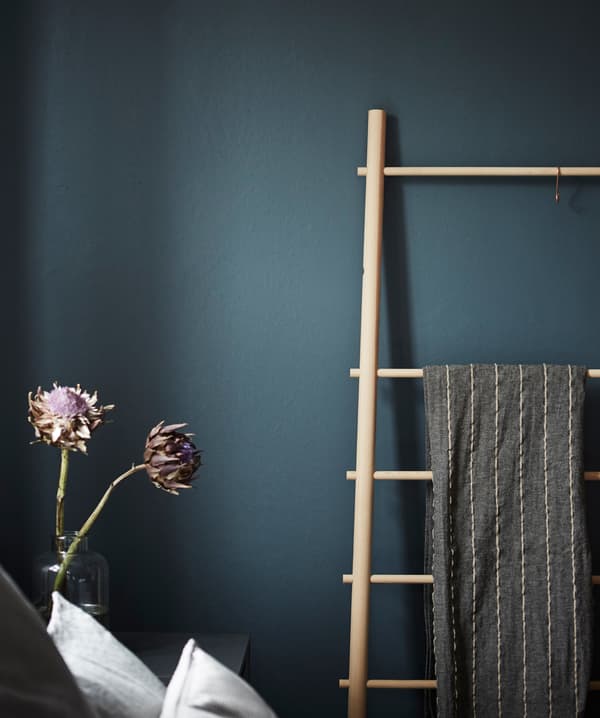 Échelle porte-serviettes en bois appuyée contre un mur foncé, dans une chambre.