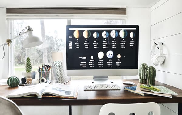 Écran d’ordinateur sur un bureau, avec cahiers, classeurs et une lampe.