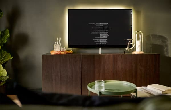 Écran TV mural avec bandeau lumineux à l'arrière pour adoucir les contrastes lorsque la pièce est plongée dans l'obscurité.