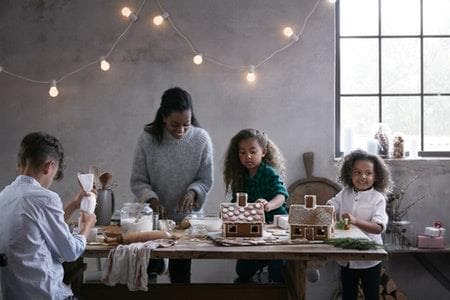 A woman with three kids decorating gingerbread houses.