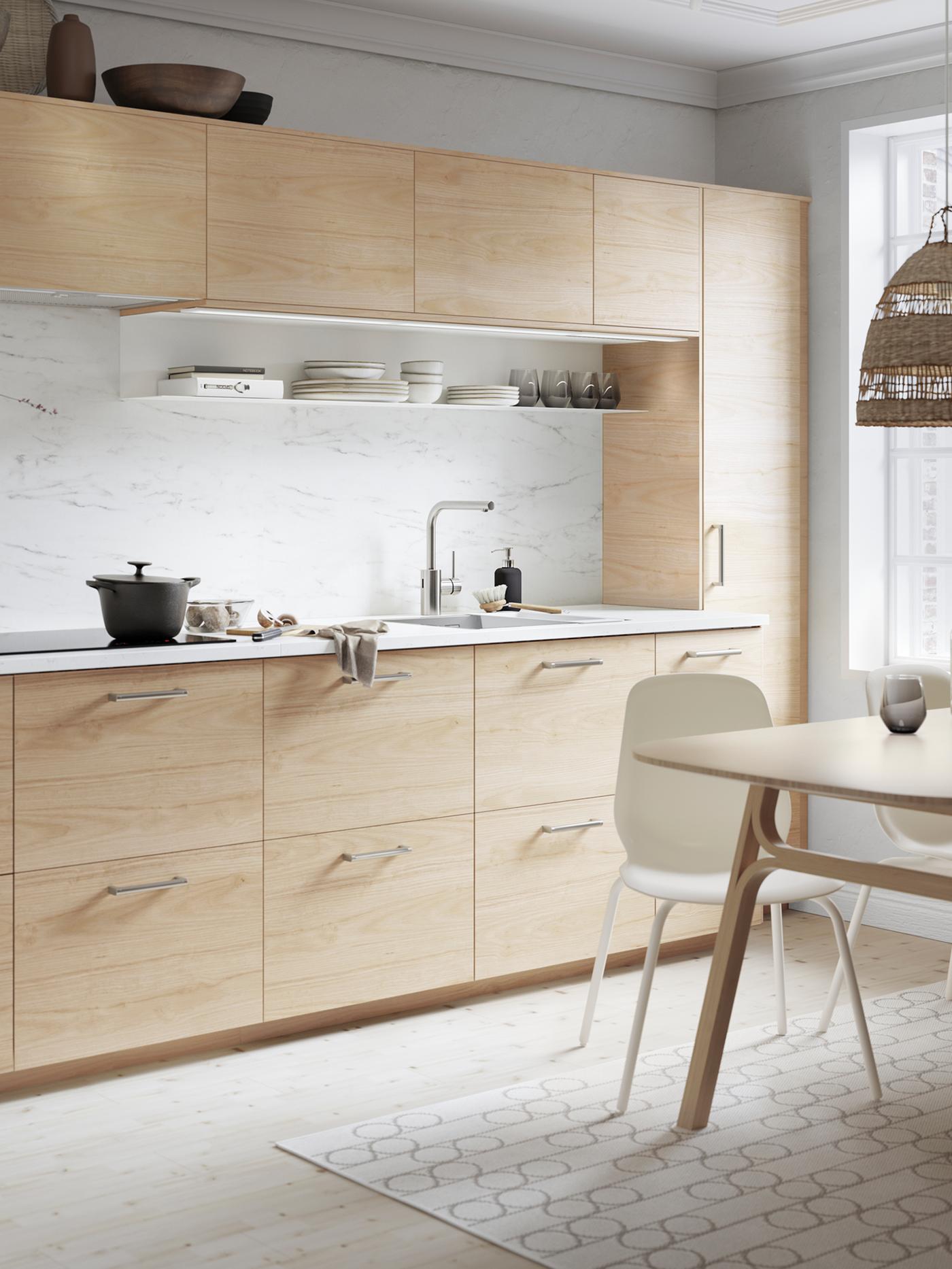 Een ASKERSUND keuken in licht esseneffect met een EKBACKEN werkblad in wit marmereffect. Op de kookplaat staat een braadpan.