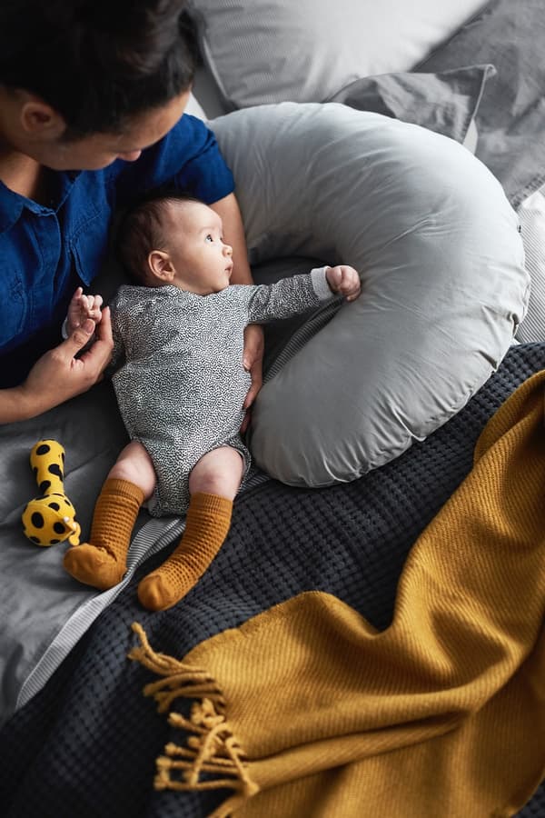 Een baby ligt in de armen van een vrouw ondersteund door een LEN voedingskussen