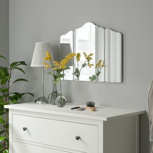 Een barok spiegel in sierlijke vormen hangend aan de muur boven een kastje. 