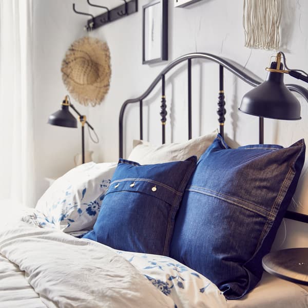 Een bed met twee IKEA SISSIL kussenovertrekken in blauwe denim tussen allerlei andere kussens.