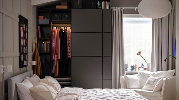 Een beige slaapkamer met kledingkast met donkergrijze schuifdeuren die half open staan