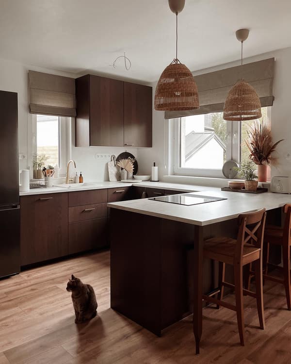 Een bruine keuken met een schiereiland en een licht aanrechtblad. Boven de keuken hangen twee rotan hanglampen.