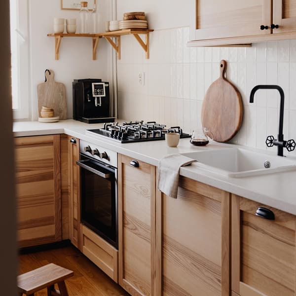 Een bruine keuken met houten fronts en zwarte handgrepen, een wit aanrechtblad en een zwarte kraan.
