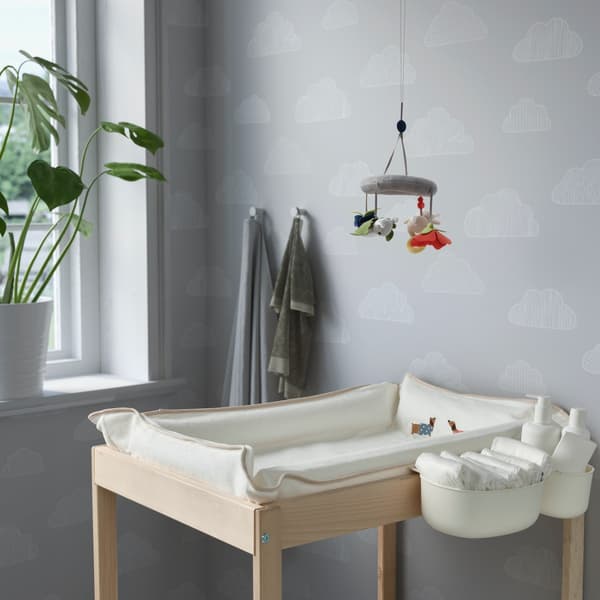 Een commode met een aankleedkussen erop en aan de commode hangen bakjes met luiers.
