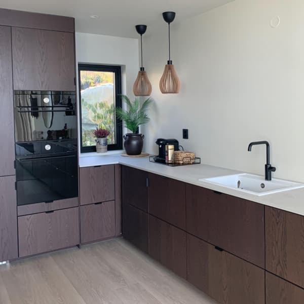 Een donkerbruine keuken met een wit aanrechtblad en een zwarte kraan.