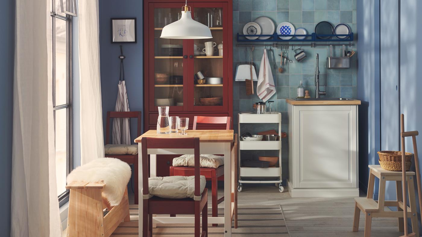 Een eetkamer in Zweedse cottagestijl met betegelde blauwe wanden, rood gebeitste PINNTORP stoelen en meubels in traditionele stijl.