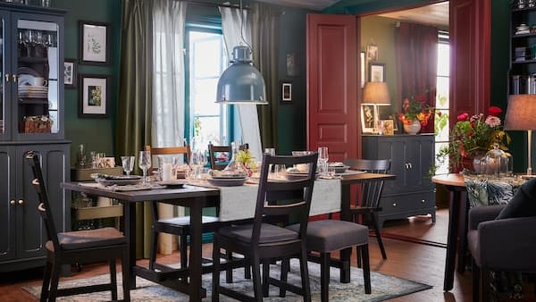 Een eetkamer met een tafel en vijf stoelen in het zwart, een oosters tapijt en een grijs-turquoise hanglamp.