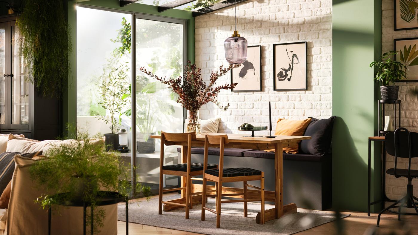 Een eetkamer met veel planten en een NACKANÄS eettafel en stoelen voor een bank en naast een terrasdeur.