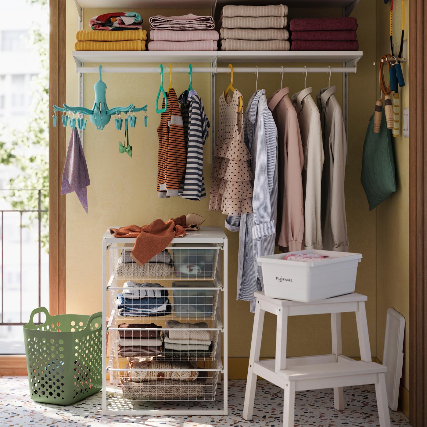 Een gele badkamer met een witte BOAXEL kledingkastcombinatie heeft witte dozen op planken en kleding die aan een rail hangt.
