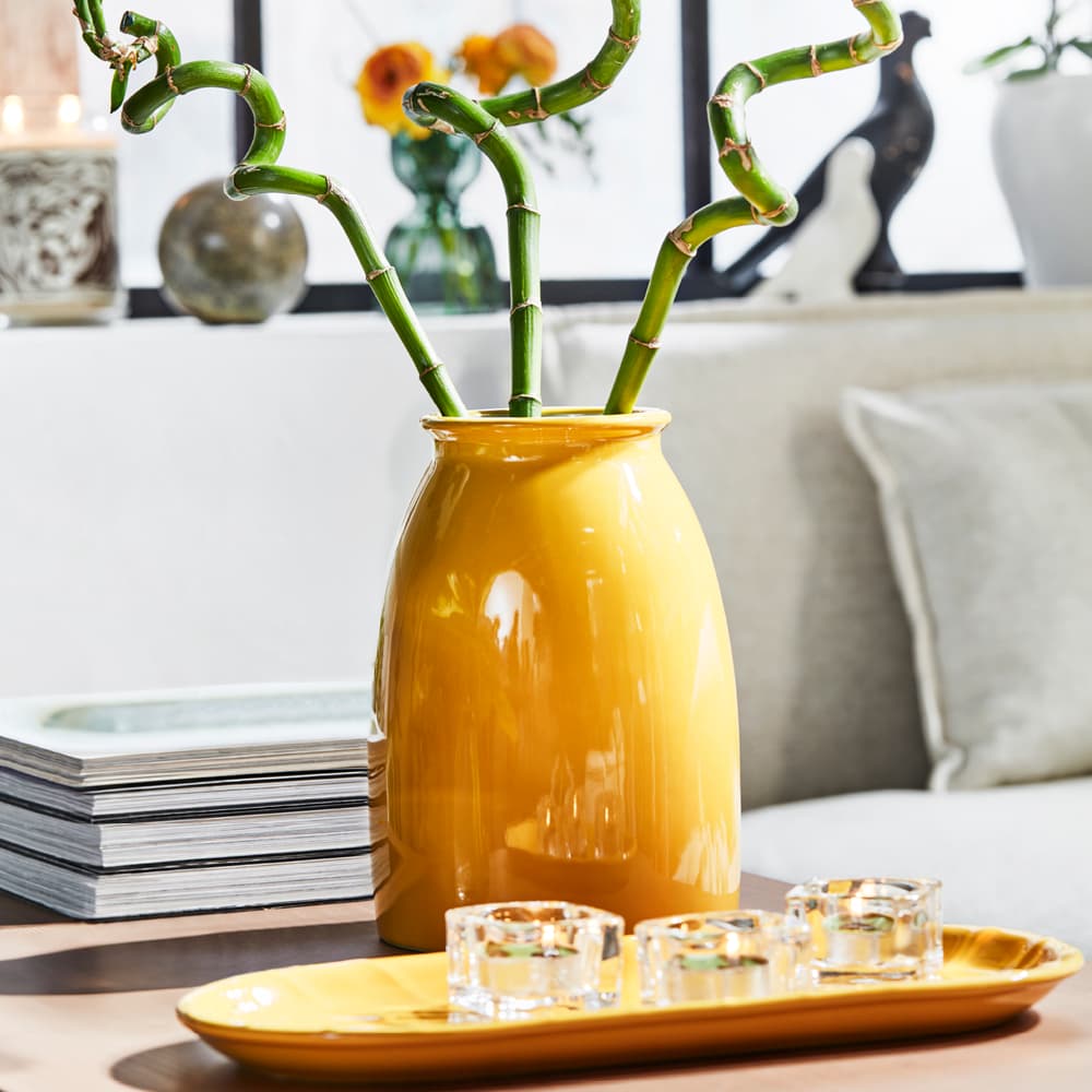 Een gele vaas met daarin bloemen en daarvoor een klein serveerschaaltje