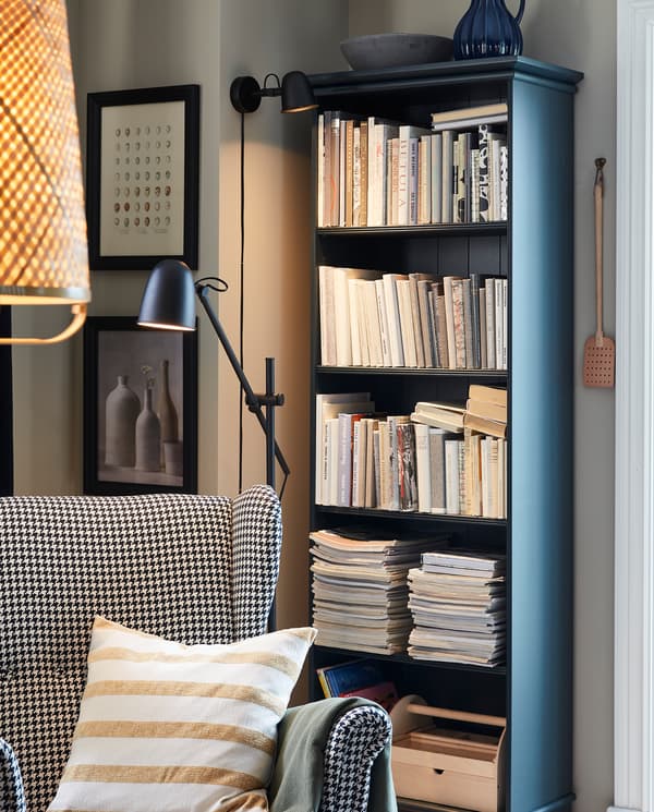 Een gezellig leeshoekje met een SKURUP wandlamp, een SKURUP staande lamp, een oorfauteuil en een boekenkast in donker blauwgroen.