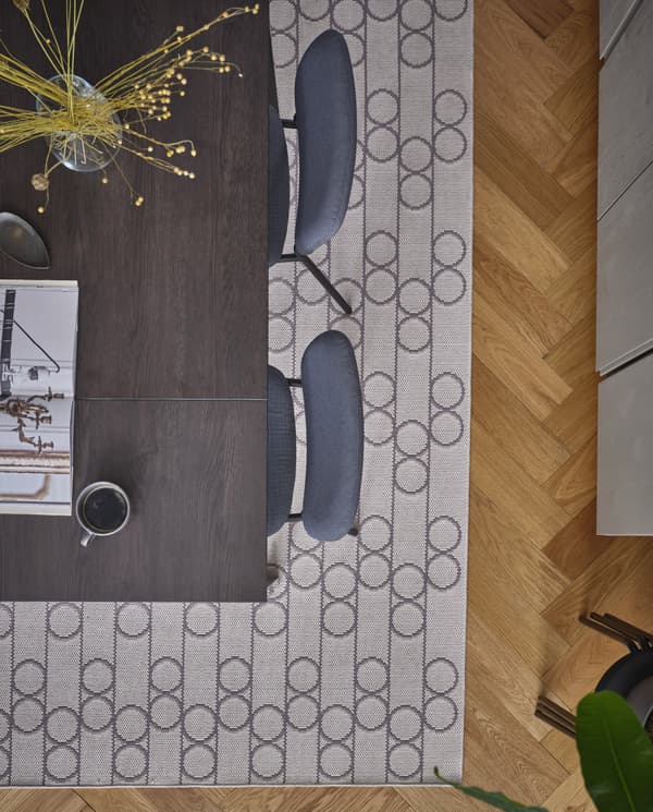 Een gladgeweven kleed met een geometrisch patroon met cirkels onder een zwartbruine eettafel met grijze stoelen.