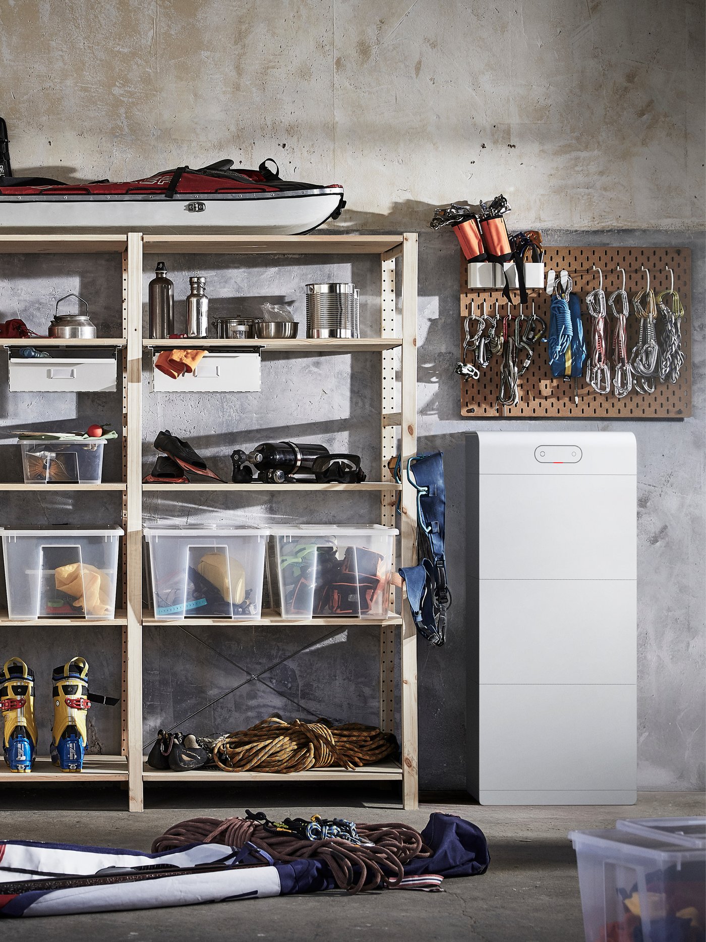 Een goed georganiseerde opslagruimte, waarschijnlijk in een garage of werkplaats, ingericht voor buiten- en klimmateriaal. Rechts van de kast staat een wit rechthoekig apparaat, waarschijnlijk een accu-opslagsysteem of voedingseenheid.