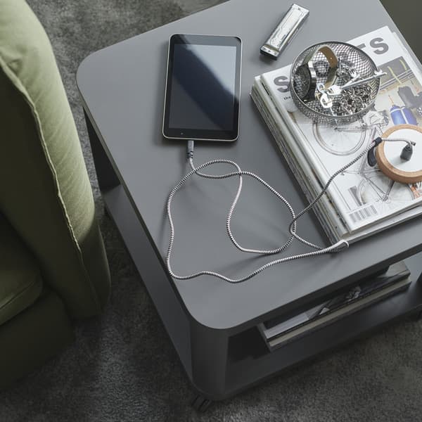 Een grijze bijzettafel, een gaaskom met sleutels en een smartphone die wordt opgeladen met LILLHULT kabel met een textieloppervlak.