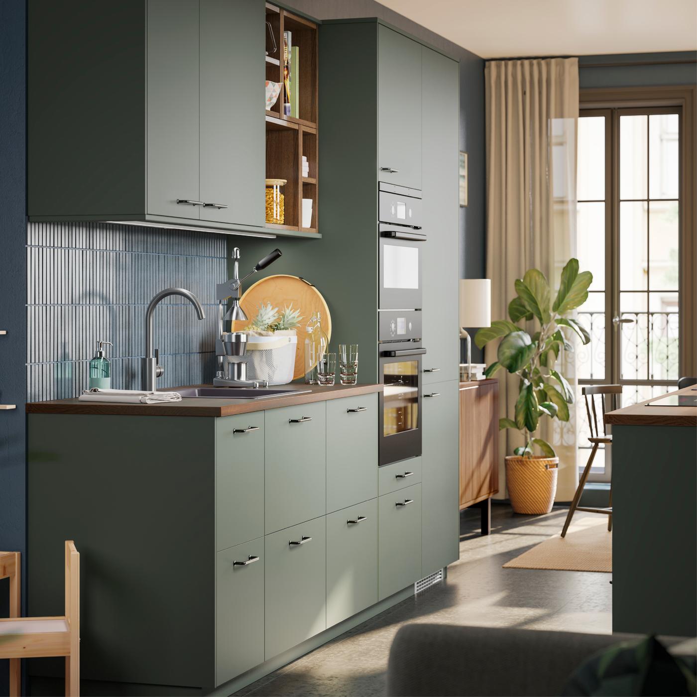 Een groene keuken met houten werkblad en zwarte apparatuur