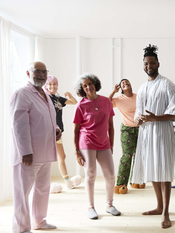 Een groep mensen gekleed in hun pyjama staan ​​allemaal glimlachend in een lichte kamer.