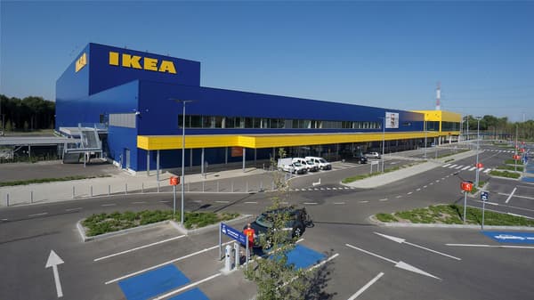 Een groot IKEA warenhuis met blauwe gevel en gele accenten, gelegen aan een brede verkeersweg met parkeerfaciliteiten ervoor.