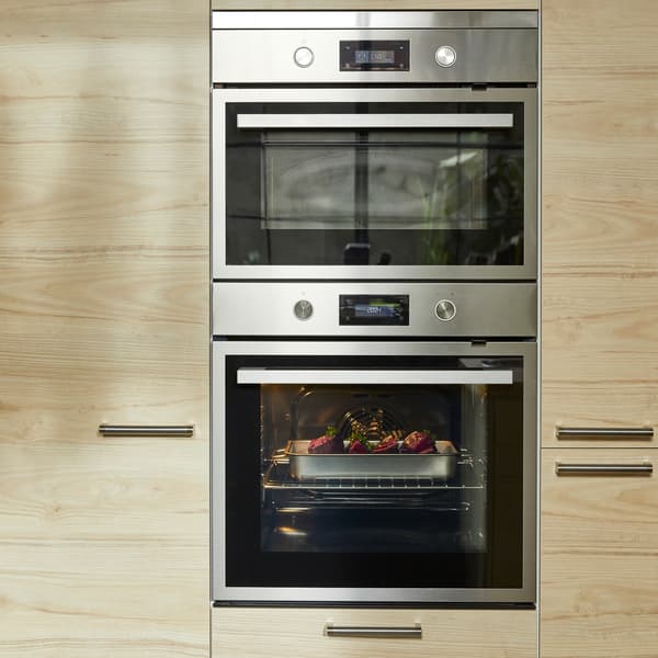Een grotere oven en een kleinere oven in zwart/roestvrij staal en ladefronten en deurfronten in licht esseneffect.