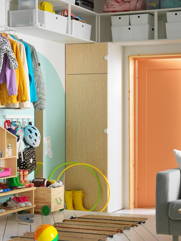 Een hal die doorloopt naar een woonkamer. Aan één kant staat een PLATSA kledingkast met daarboven open planken.