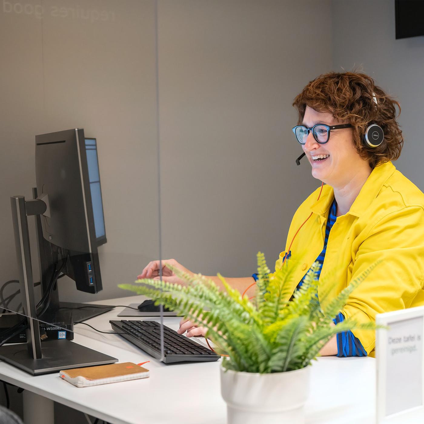 Een IKEA medewerker met een gele blouse en een koptelefoon op zit achter de computer.