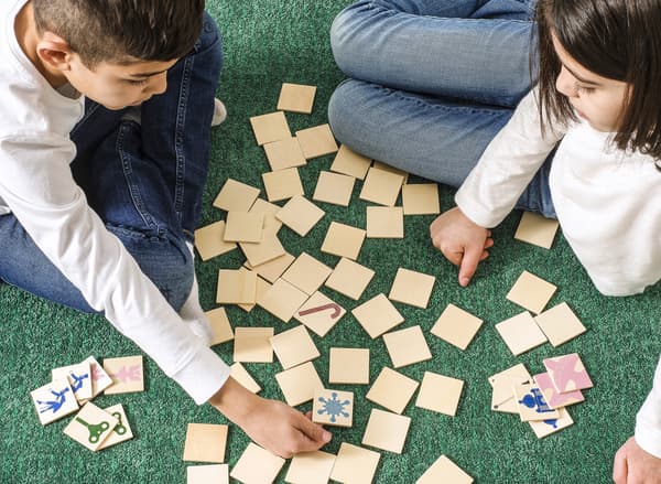 Een jongen en een meisje zitten op een groen tapijt een spelletje te spelen.