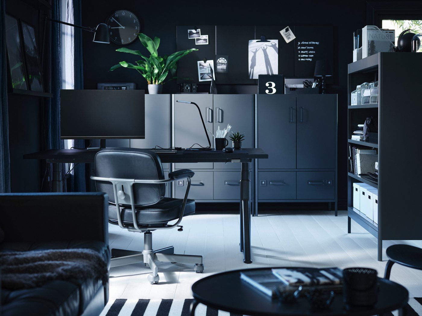 Een kamer in een zwart-wit kleurenschema, met donkergrijze IDÅSEN opbergmeubels die een donkergrijs IDÅSEN zit-sta bureau omlijsten.