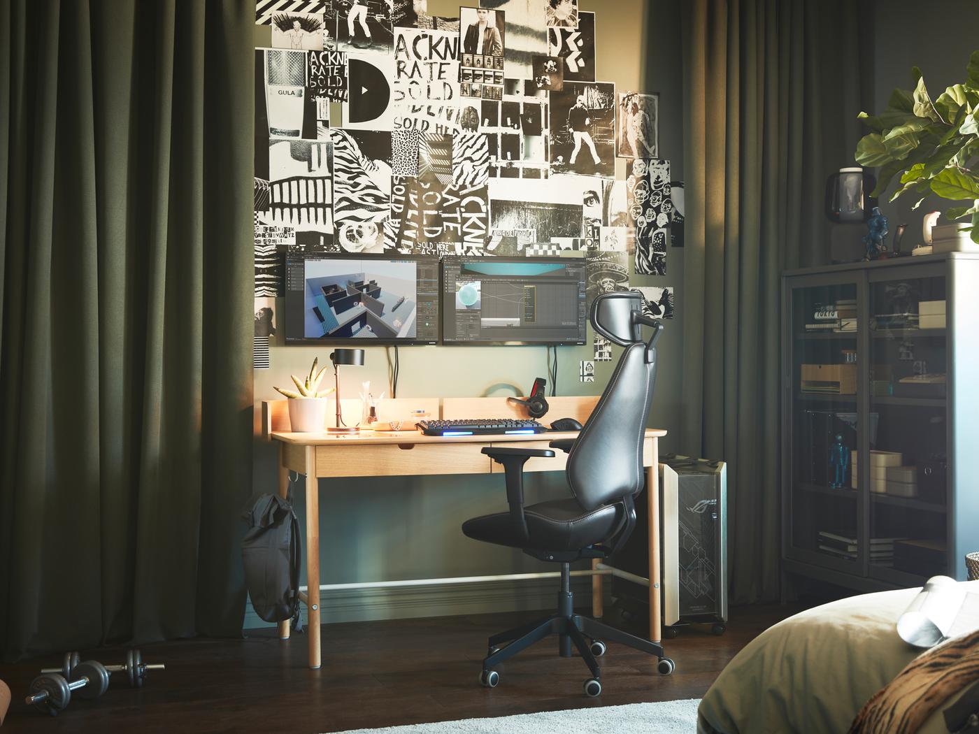 Een kamer waar de kleur groen de boventoon voert met een RIDSPÖ bureau in eiken fineer naast donkergroene ROSENMANDEL gordijnen die open staan zodat schermen en prenten aan de wand zichtbaar zijn.