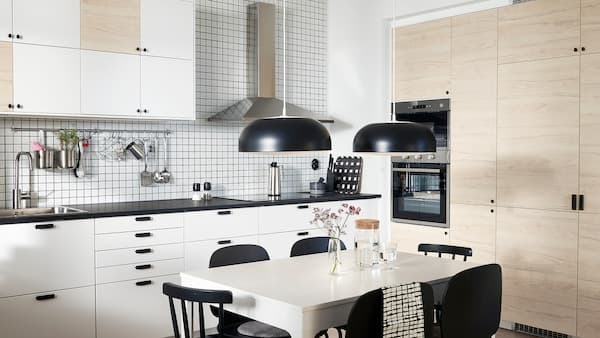 Een keuken met fronten in het wit en licht esseneffect, twee zwarte hanglampen, een witte tafel en zwarte stoelen.