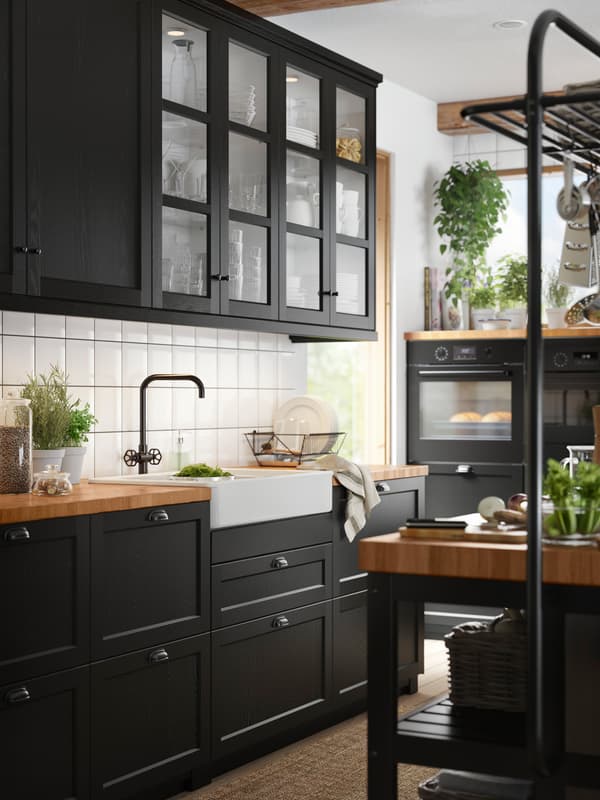 Een keuken met glazen deuren met een zwart gebeitst frame, kasten met zwart gebeitste fronten en een houten werkblad.