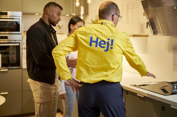 Een keukenverkoper geeft advies aan twee mensen, ze staan in een keuken.