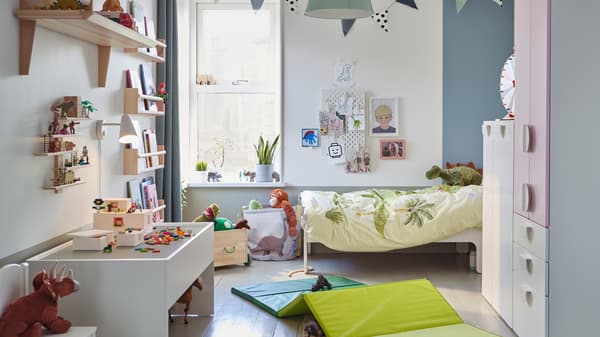 Een kinderkamer met een SLÄKT meegroeibed in de hoek en SMÅSTAD opbergsysteem tegenover een DUNDRA speeltafel.