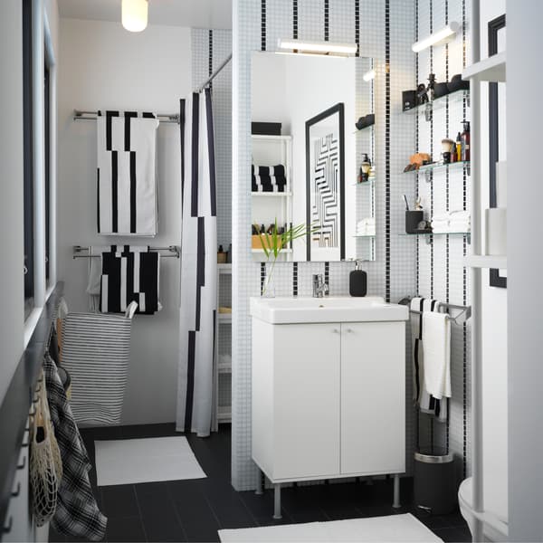 Een kleine badkamer in zwart/wit met een witte wastafel, gestreepte handdoeken en een gestreept douchegordijn.