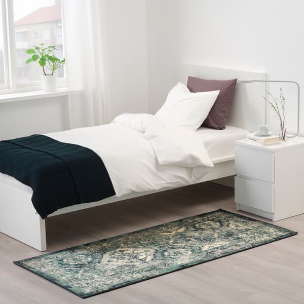 Een laagpolig vintage vloerkleed met een groen en geel motief in een slaapkamer met een bed en een nachtkastje.