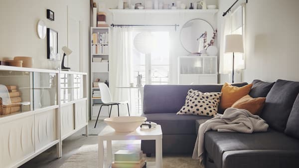 Een luchtige, lichte woonkamer met een FRIHETEN slaapbank met textiel en naast elkaar staande witte KALKNÄS kasten met schuifdeuren.