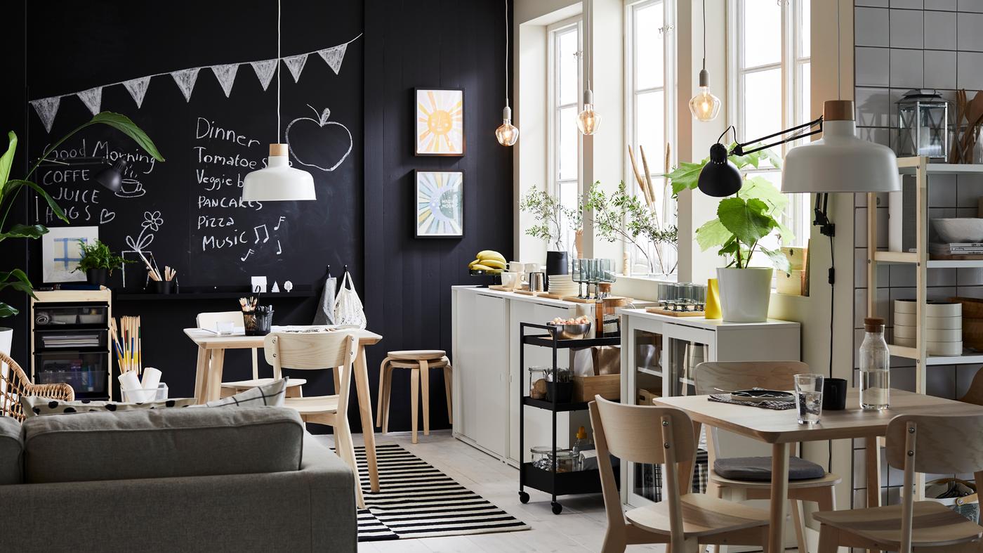 Een lunchroom met drie grote ramen en een wand met een krijtbord staan twee LISABO tafels in essenfineer met bijpassende stoelen.