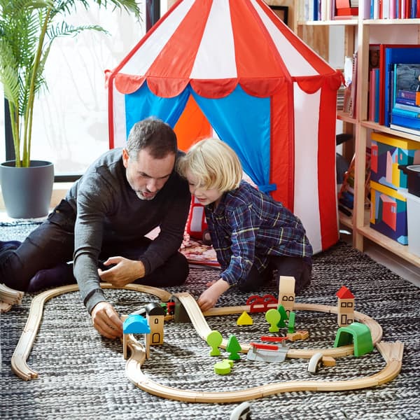 Een man en een jongetje spelen met een houten treinset voor kinderen.